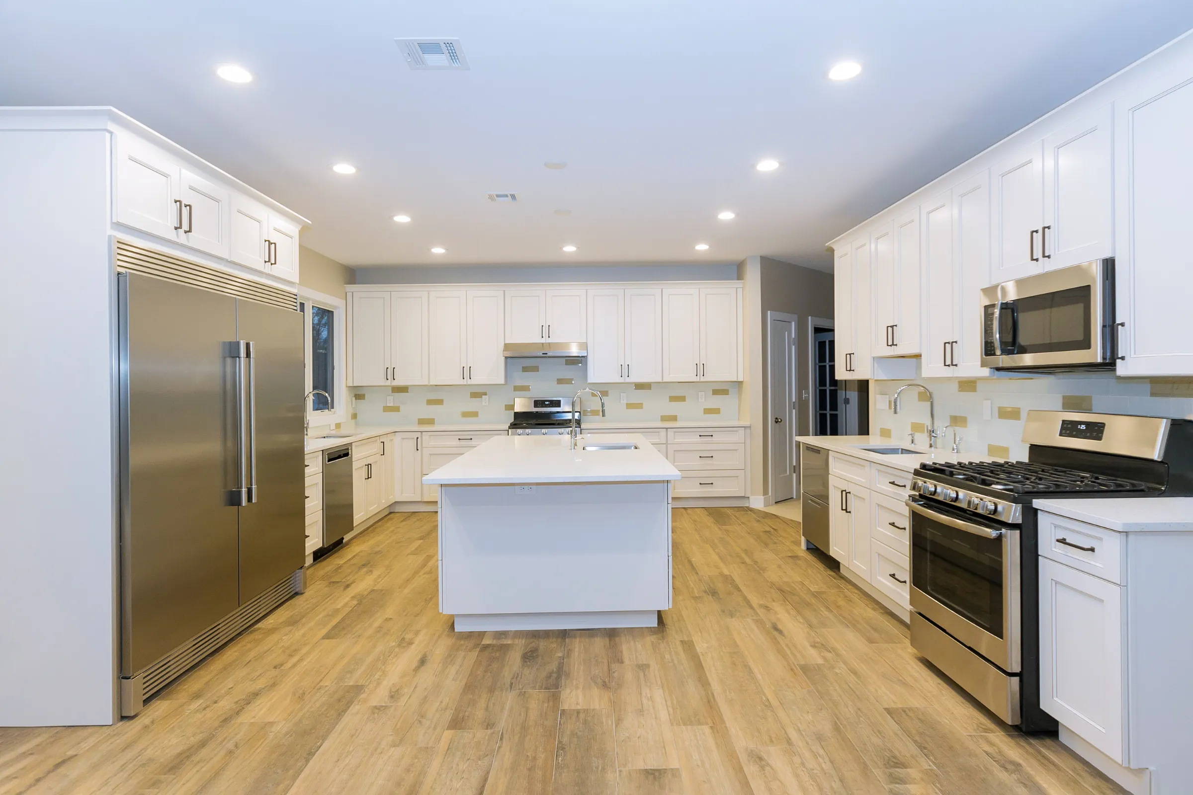 After kitchen remodeling project in Los Angeles with white shaker cabinets, center island, stainless steel appliances, recessed lighting, updated flooring, and improved kitchen layout